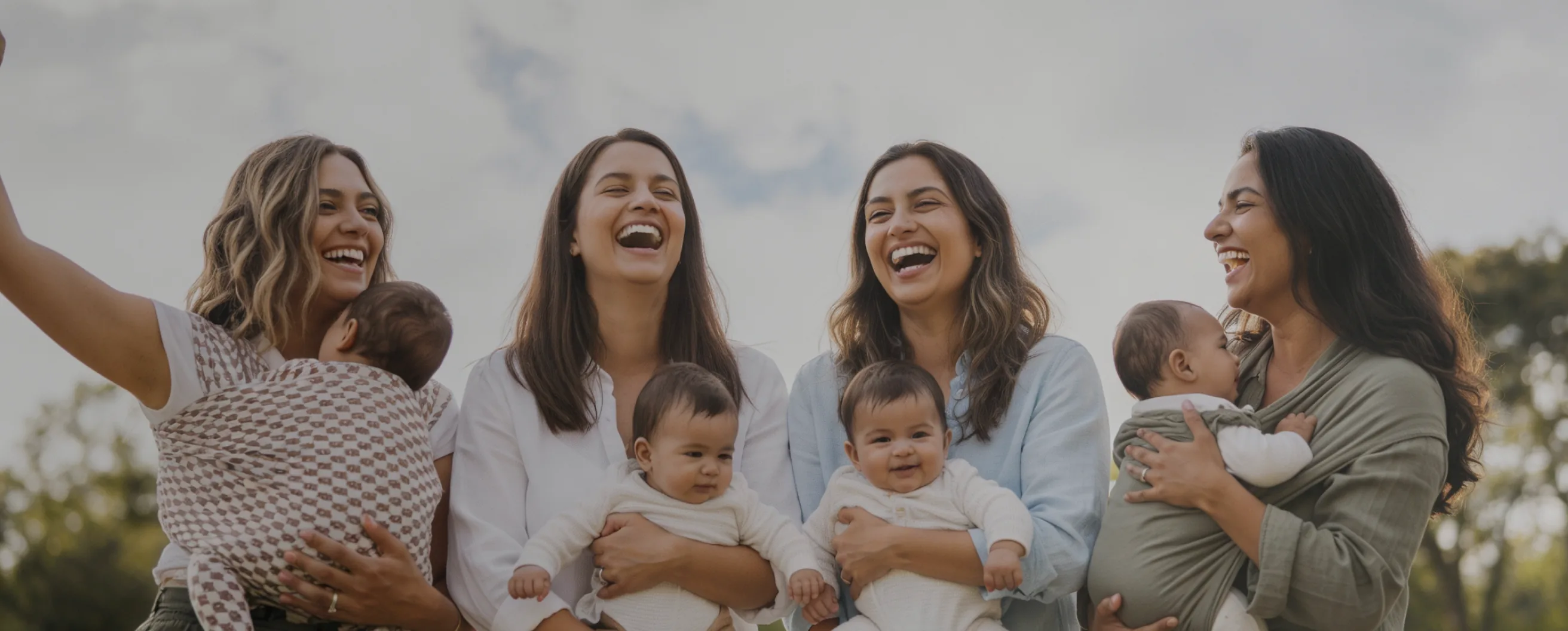 Mothers laughing together while holding their babies outdoors