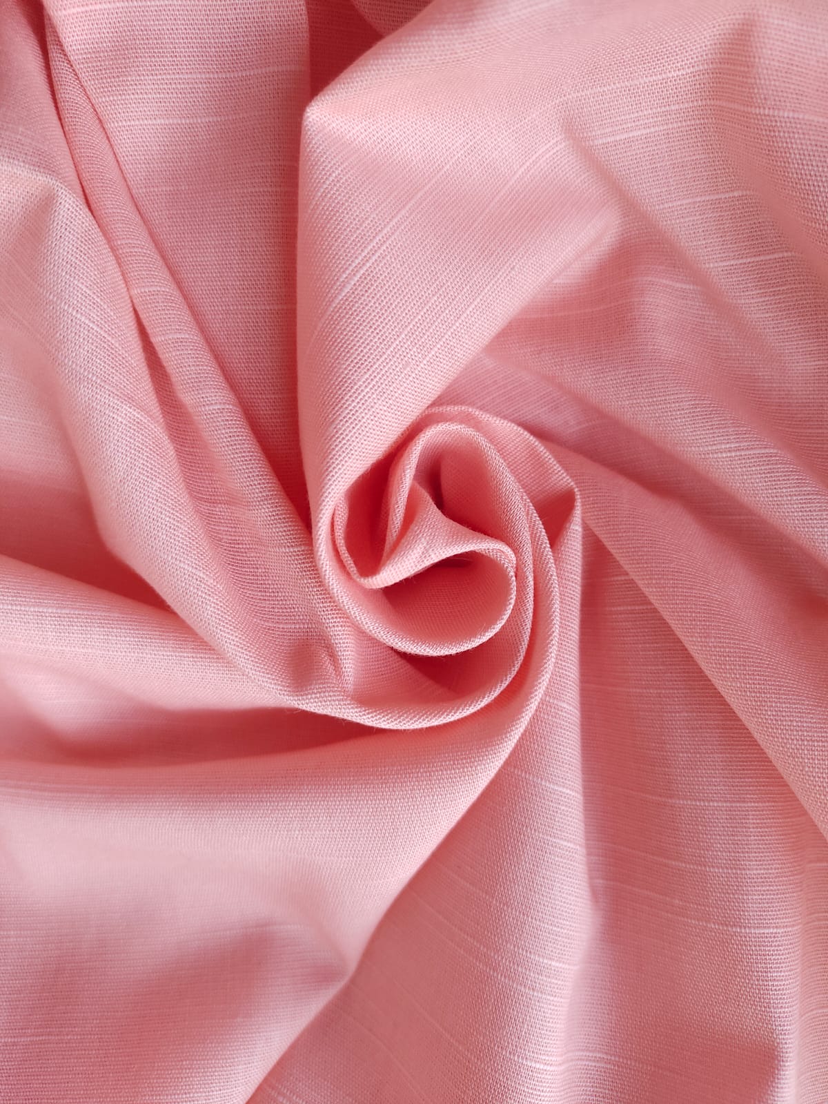 Close-up of soft, wrinkled pink cotton fabric displaying fine weave texture.