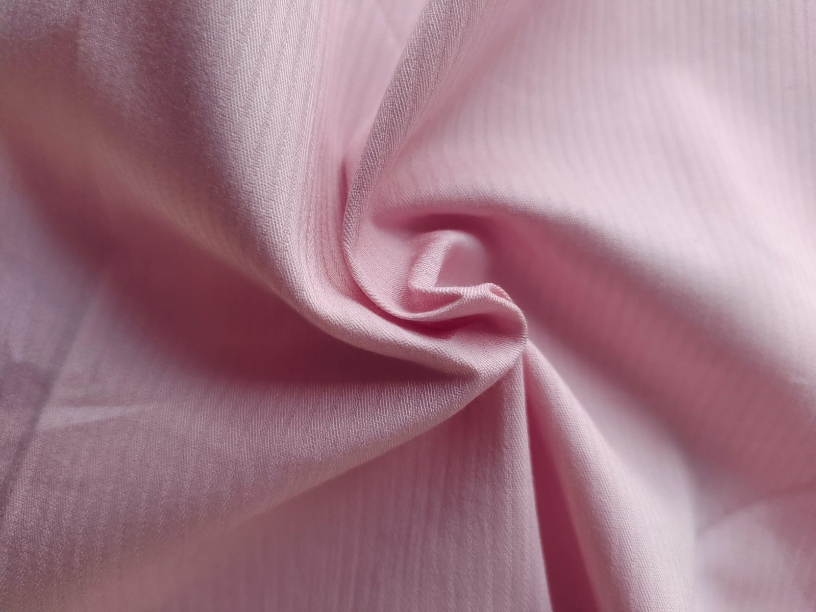 Close-up of soft, wrinkled pink cotton fabric displaying fine weave texture.