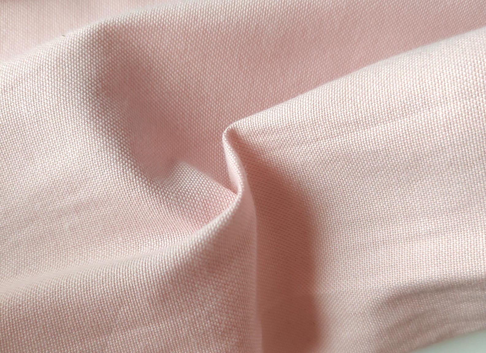 Close-up of soft, wrinkled pink cotton fabric displaying fine weave texture.