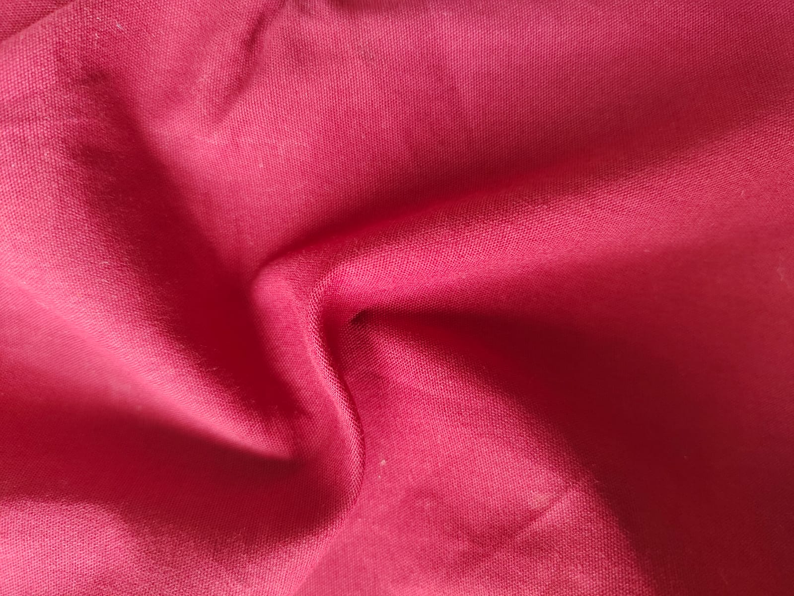 Close-up of soft, wrinkled pink cotton fabric displaying fine weave texture.