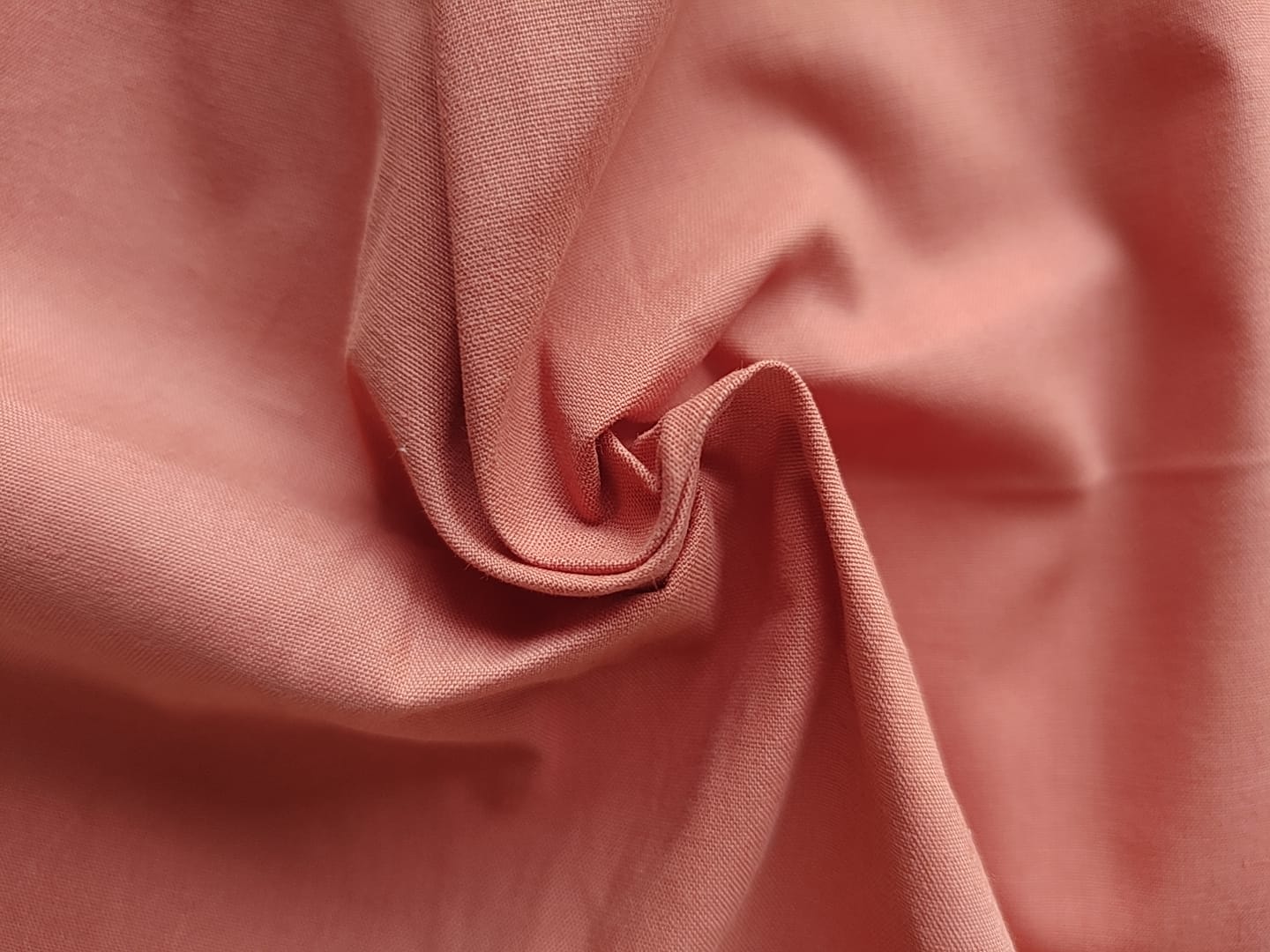 Close-up of soft, wrinkled pink cotton fabric displaying fine weave texture.