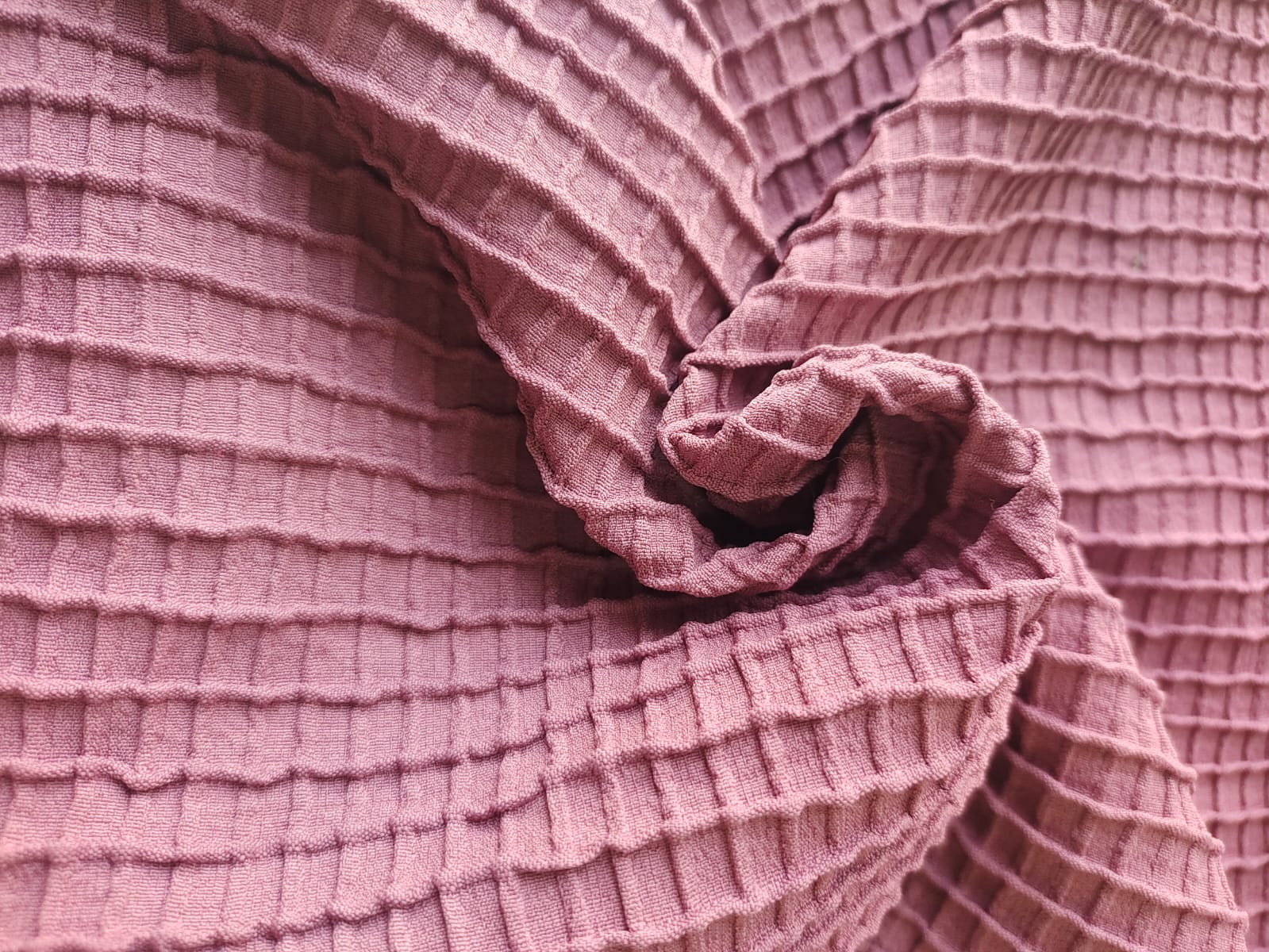 Close-up of soft, wrinkled pink cotton fabric displaying fine weave texture.