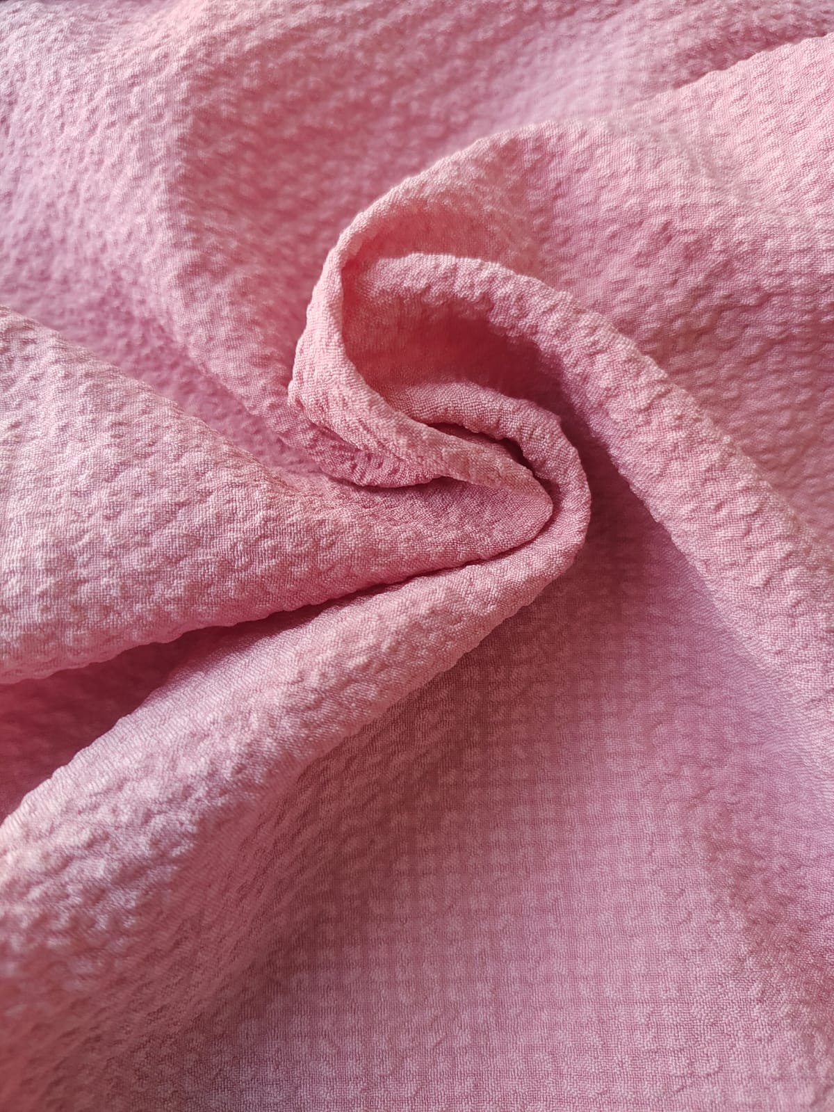 Close-up of soft, wrinkled pink cotton fabric displaying fine weave texture.