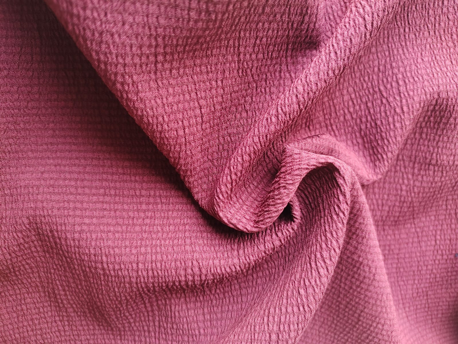 Close-up of soft, wrinkled pink cotton fabric displaying fine weave texture.