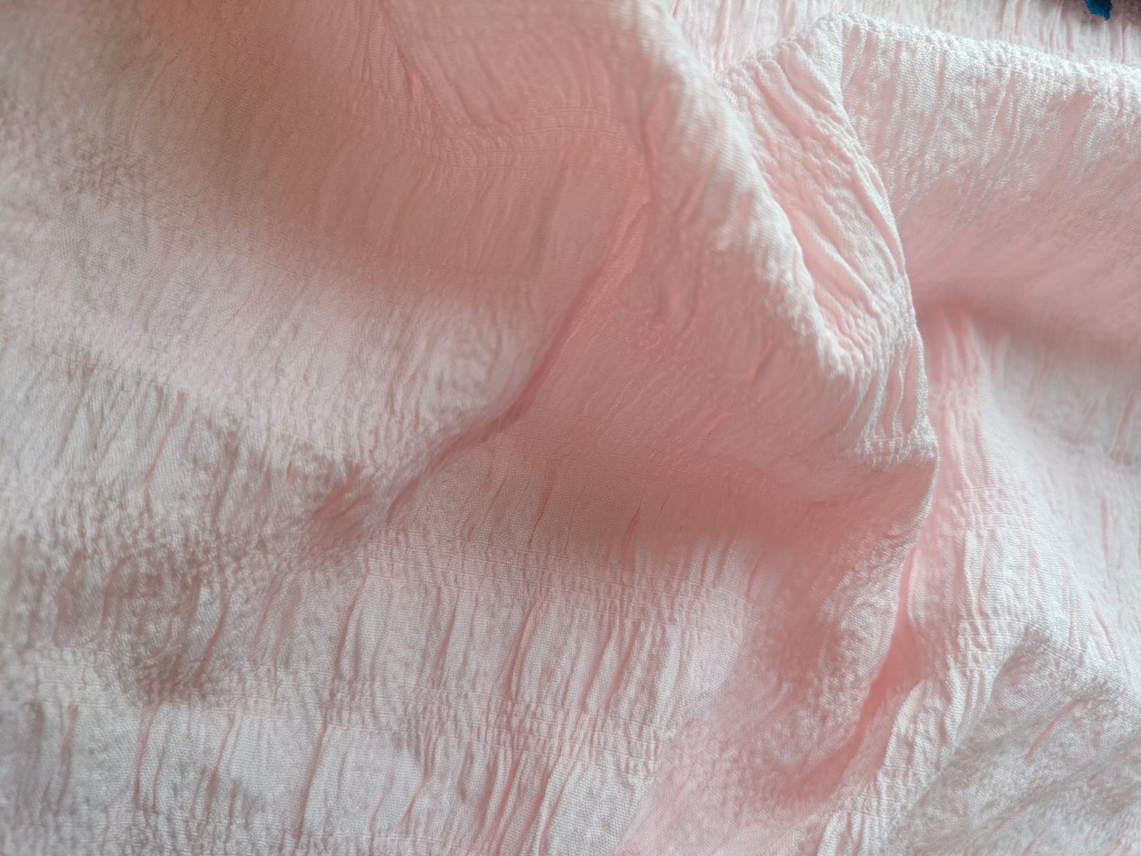 Close-up of soft, wrinkled pink cotton fabric displaying fine weave texture.