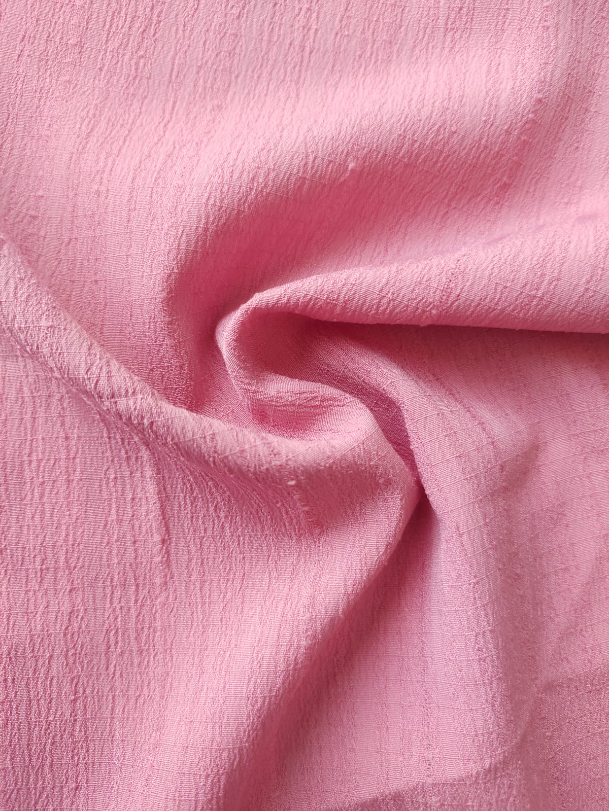Close-up of soft, wrinkled pink cotton fabric displaying fine weave texture.