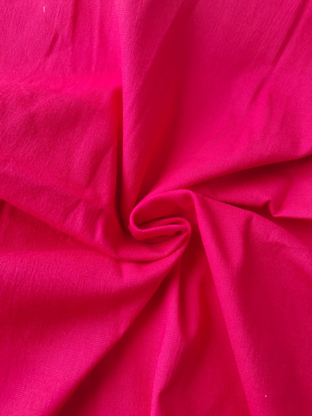 Close-up of soft, wrinkled pink cotton fabric displaying fine weave texture.