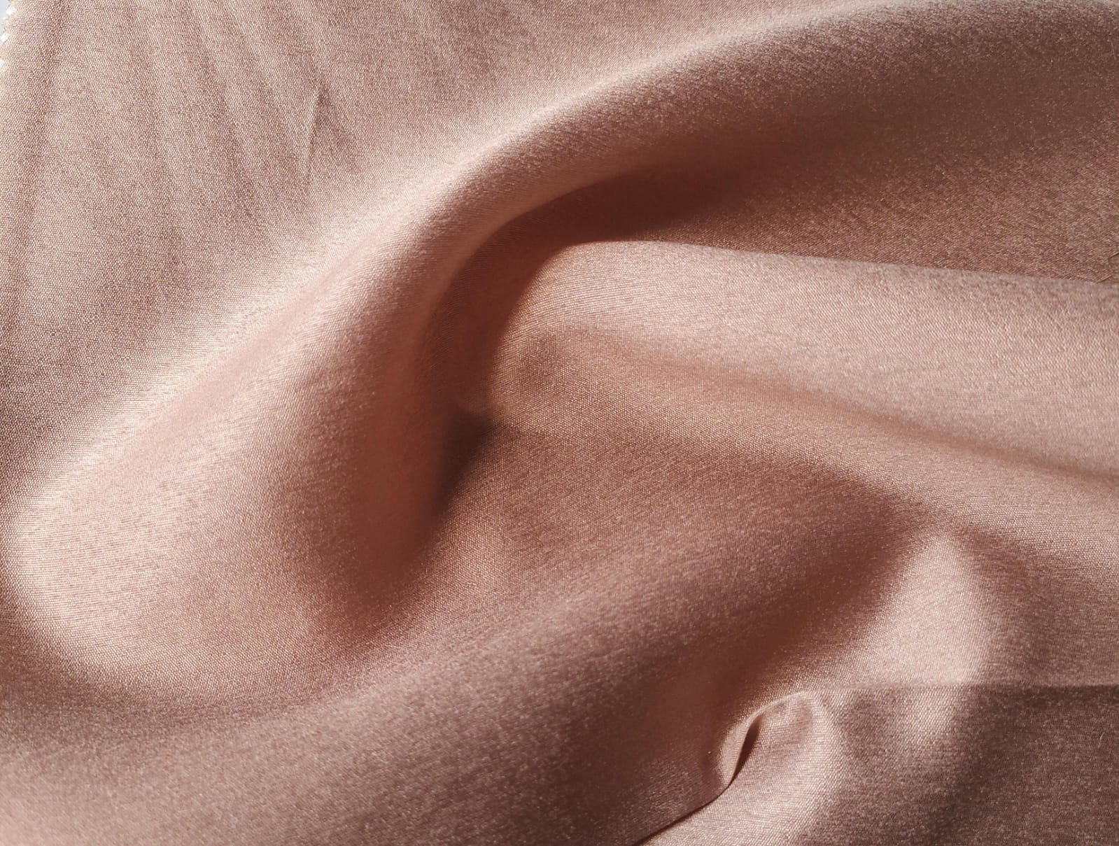 Close-up of soft, wrinkled pink cotton fabric displaying fine weave texture.
