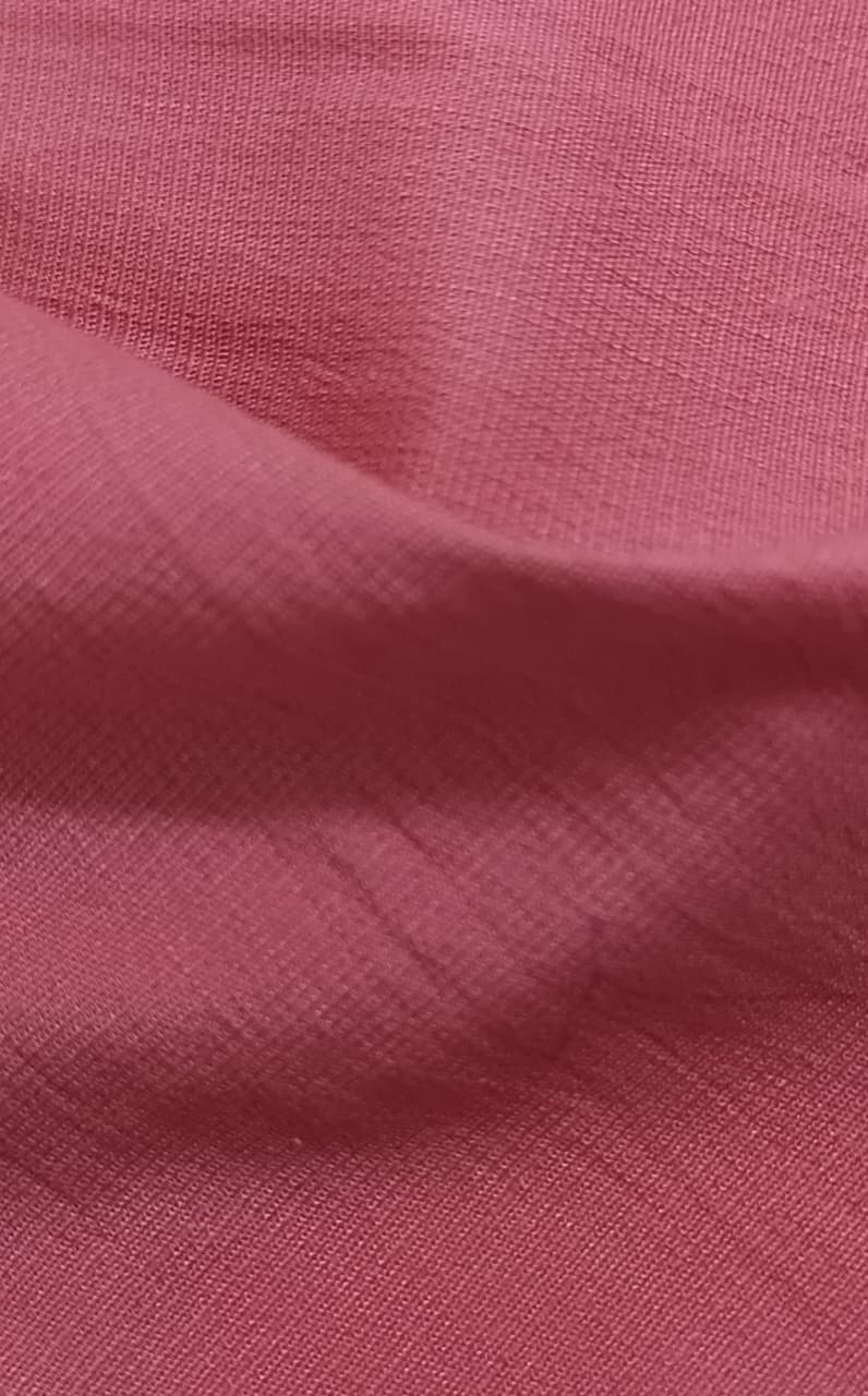 Close-up of soft, wrinkled pink cotton fabric displaying fine weave texture.