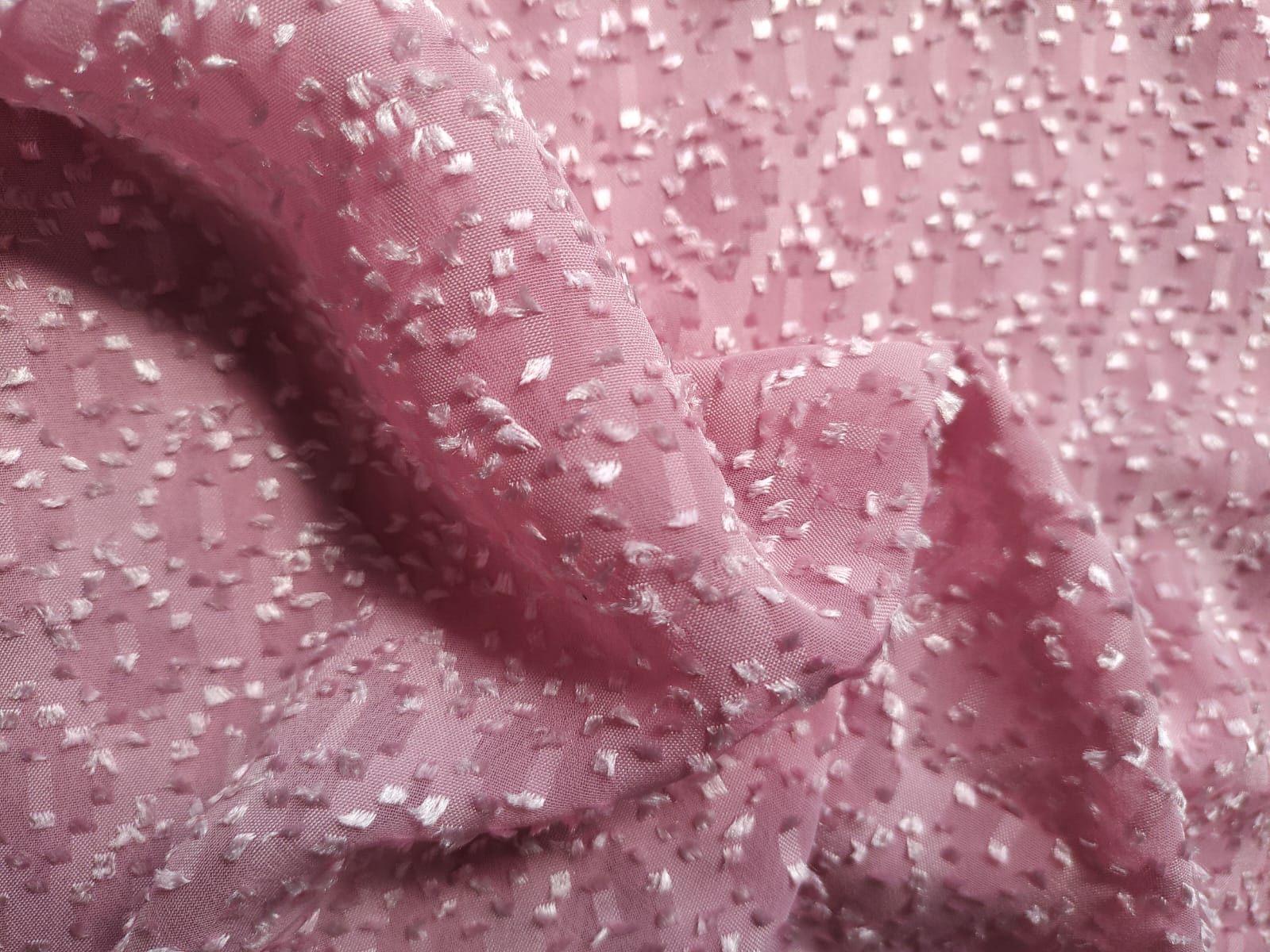 Close-up of soft, wrinkled pink cotton fabric displaying fine weave texture.