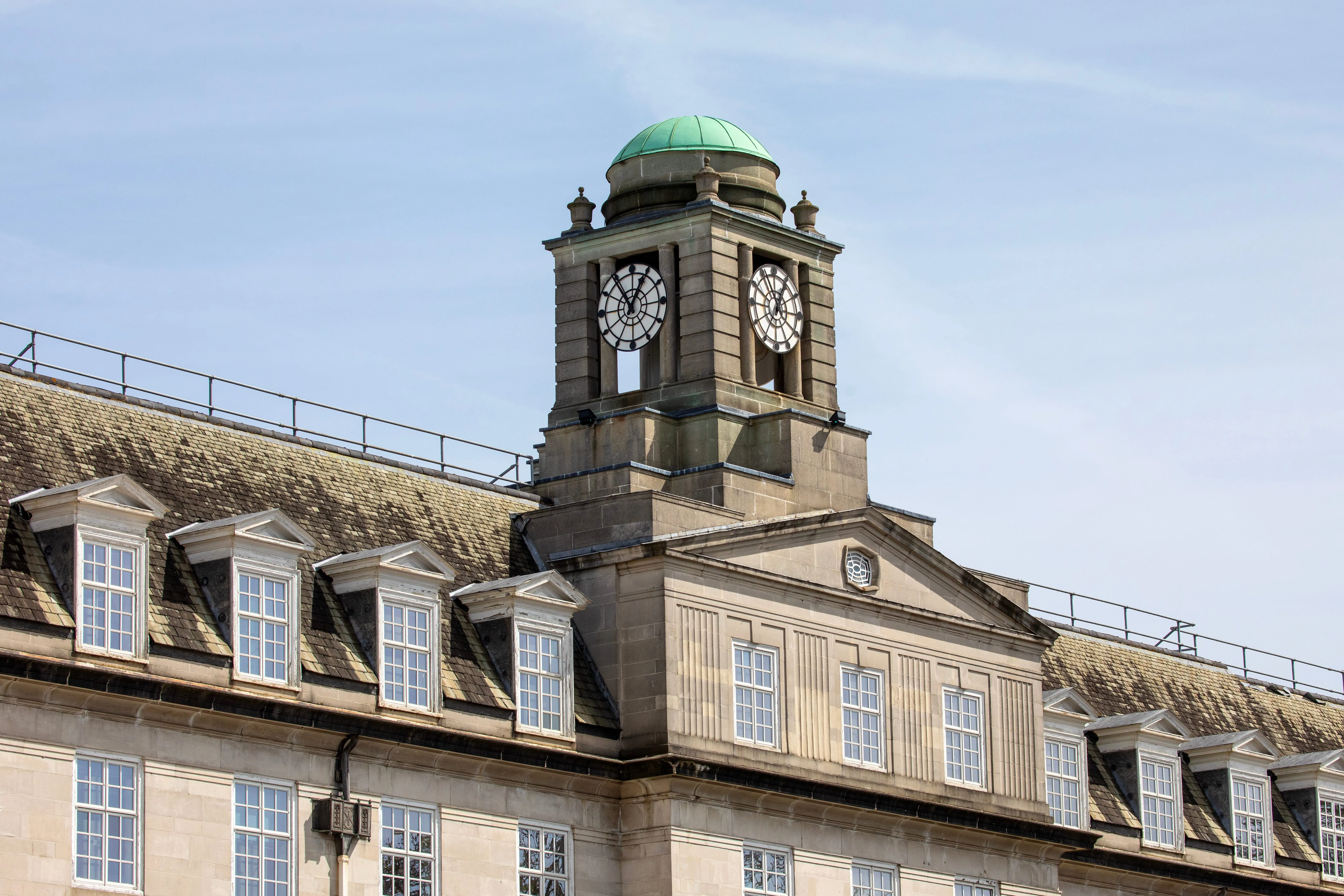 Historic stone building with green dome clock tower and mansard roof against blue sky.