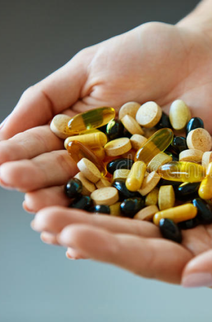 Hands holding a variety of vitamin capsules
