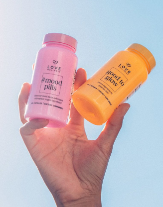 Hand holding two Love Wellness supplement bottles