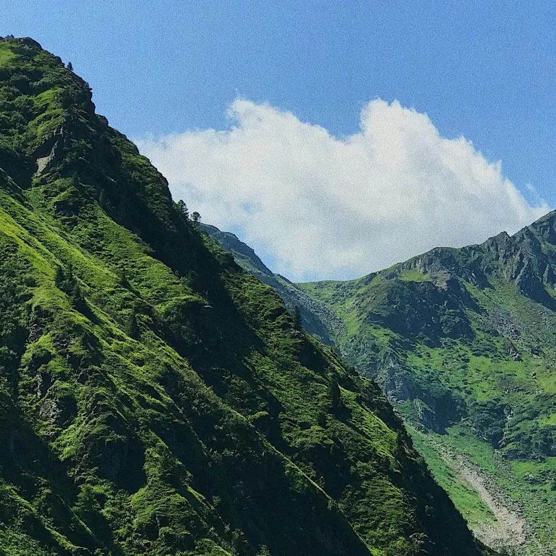Steep green mountains under a blue sky with white clouds.