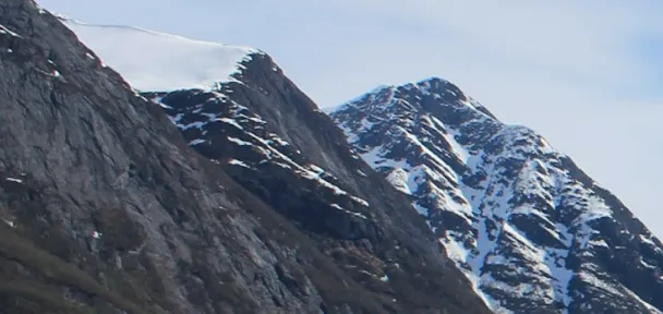 Rocky mountain peaks with patches of snow under a blue sky.
