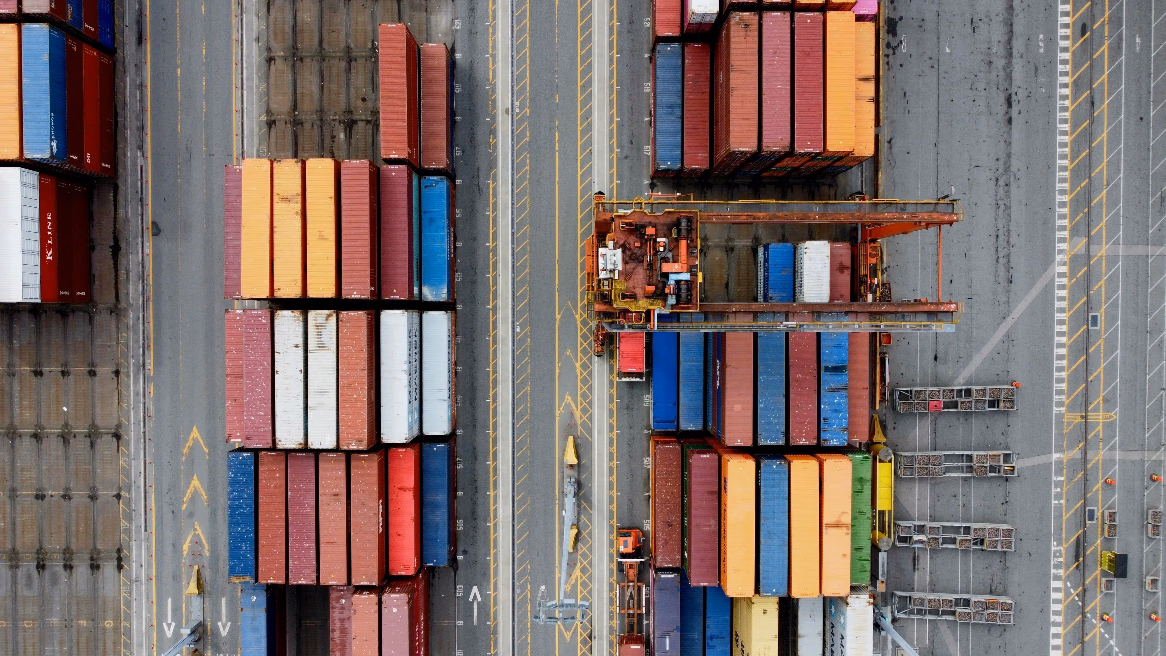 Tall stacks of colorful intermodal shipping containers at a port or logistics facility.
