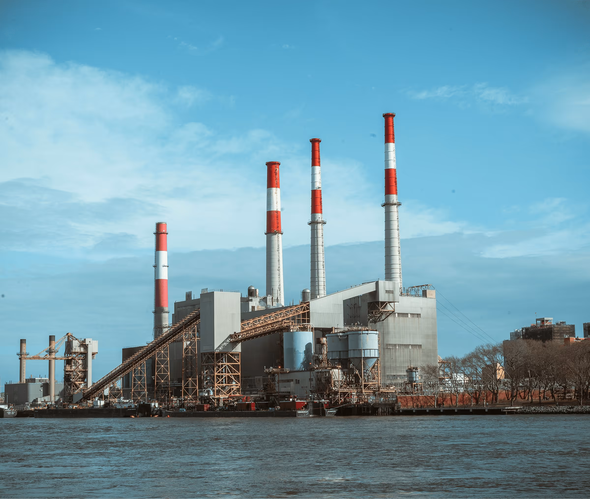 Industrial facility exterior with large equipment, pipes, and infrastructure against a clear sky.
