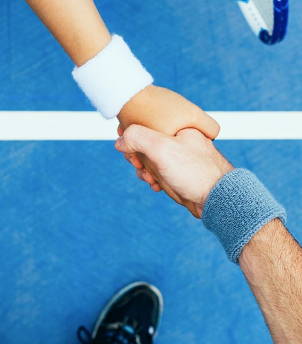 Two people shaking hands on a blue tennis court, wearing wristbands and holding tennis rackets.