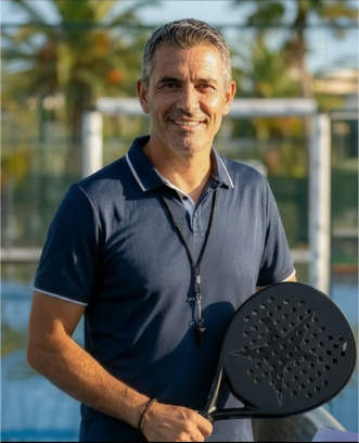 Smiling middle-aged man in navy polo shirt holding a padel racket outdoors on a sunny day.