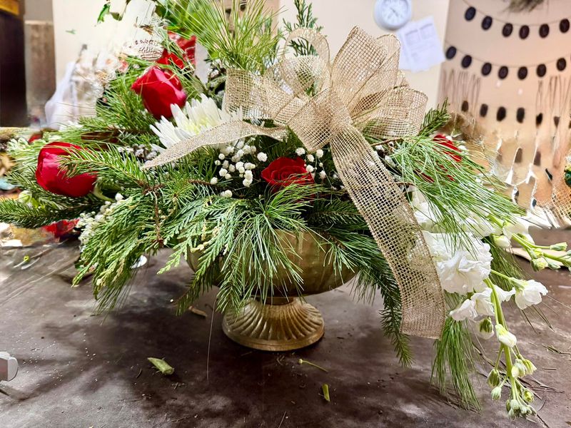 Elegant holiday centerpiece with white ribbon, red roses and evergreens
