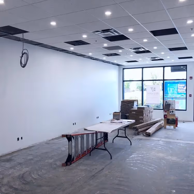 Interior of a commercial space under construction with a ladder, table, and stacked materials near a large window.