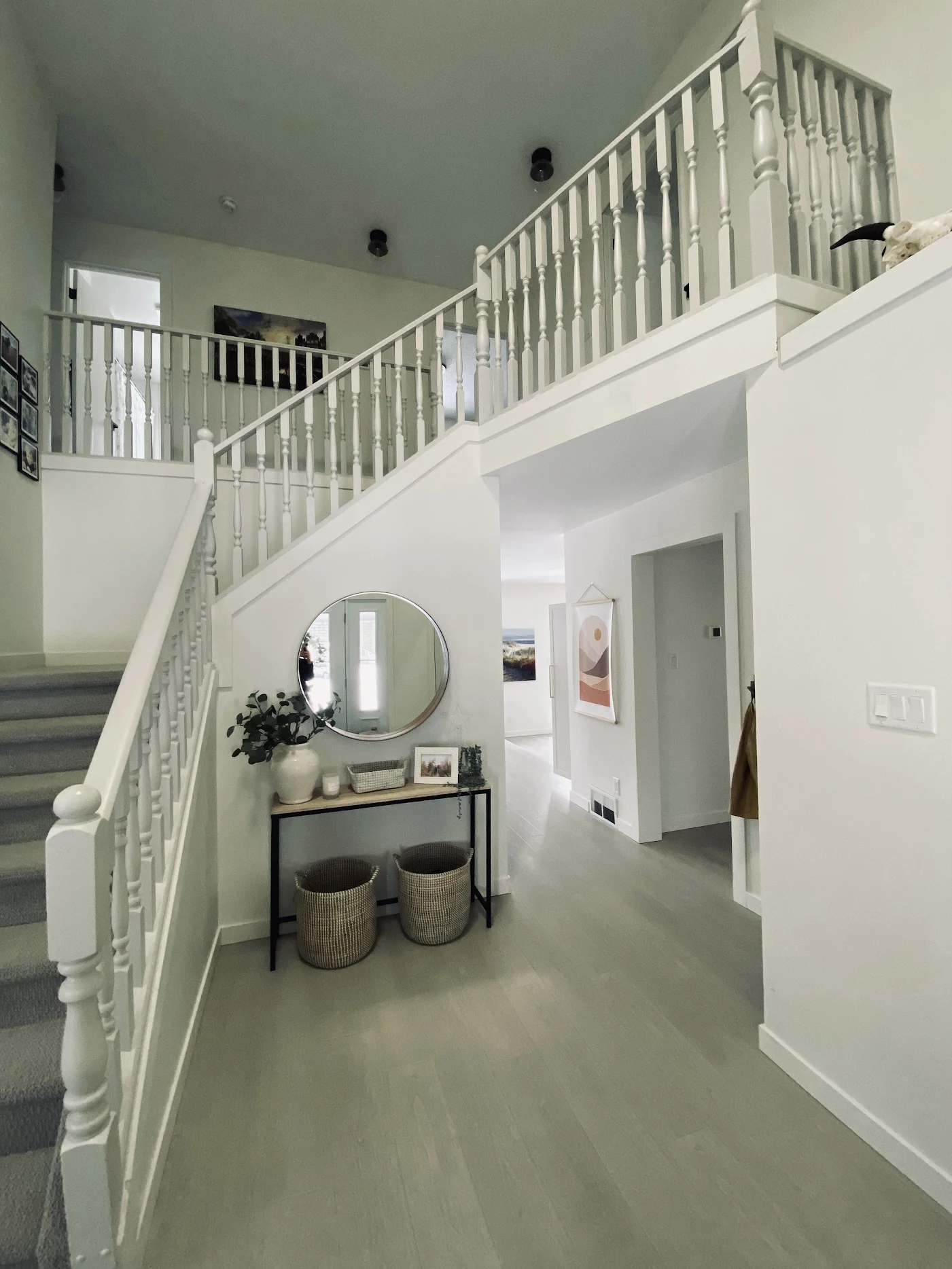 Bright home interior with white staircase, round mirror, console table, and woven baskets underneath.