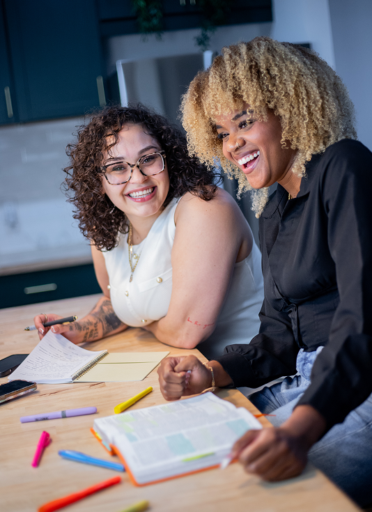 Two young women studying together at a table with notebooks, pens, and highlighters.