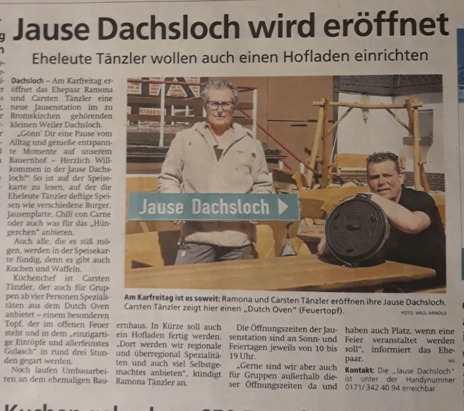 Ramona und Carsten Tänzler stehen an einem Holztisch, Carsten zeigt einen Dutch Oven, Schild weist auf Jause Dachshloch.