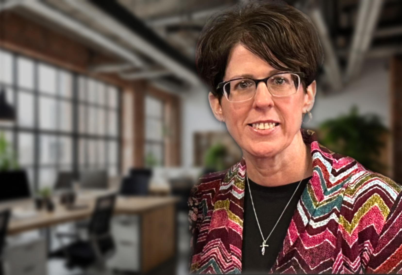 Woman with glasses wearing colorful patterned cardigan smiling in modern office