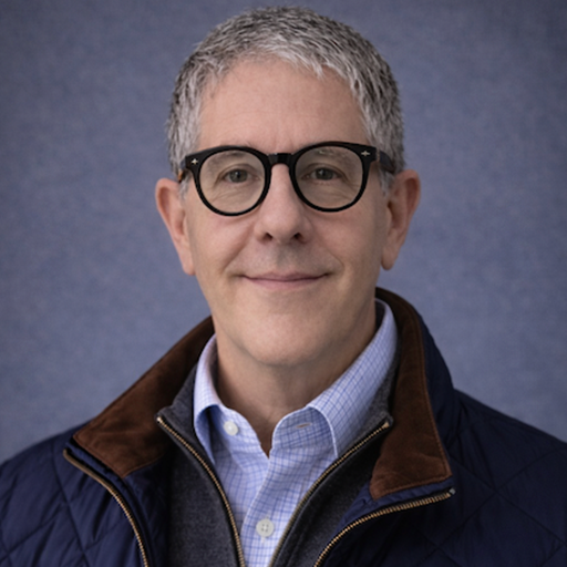Middle-aged man with gray hair and glasses wearing a blue plaid shirt and dark jacket