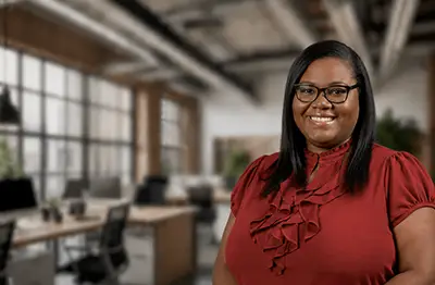 Professional woman in red blouse wearing glasses in modern office environment with large windows