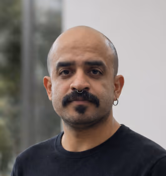 Portrait of a bald man with a mustache, septum piercing, and hoop earring wearing a black shirt.
