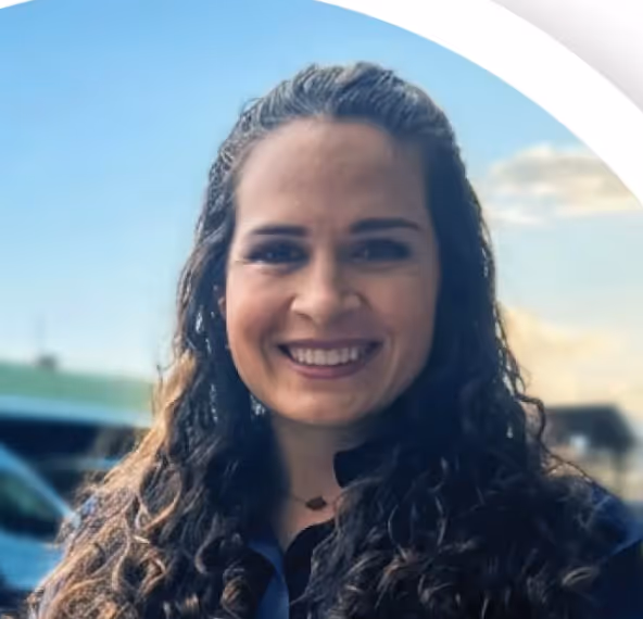 Smiling woman with long curly dark hair and a black top outdoors under blue sky.