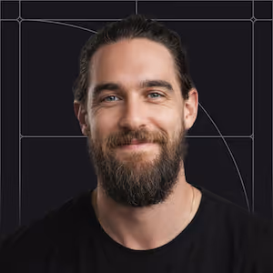 Smiling man with dark hair tied back and full beard wearing a black shirt, black background with faint lines.