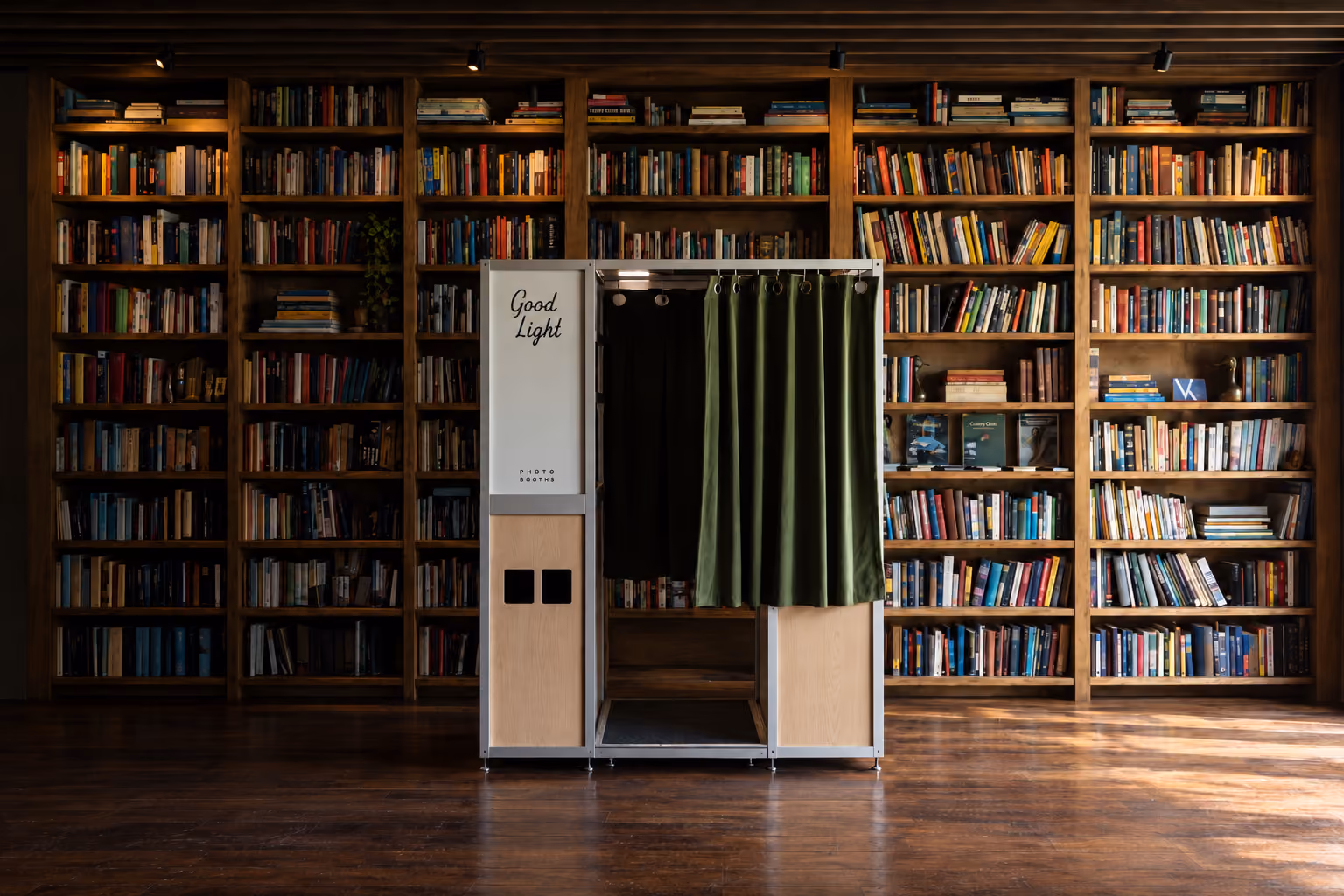 Good Light enclosed photo booth with a green velvet curtain, standing in a library lined with bookshelves