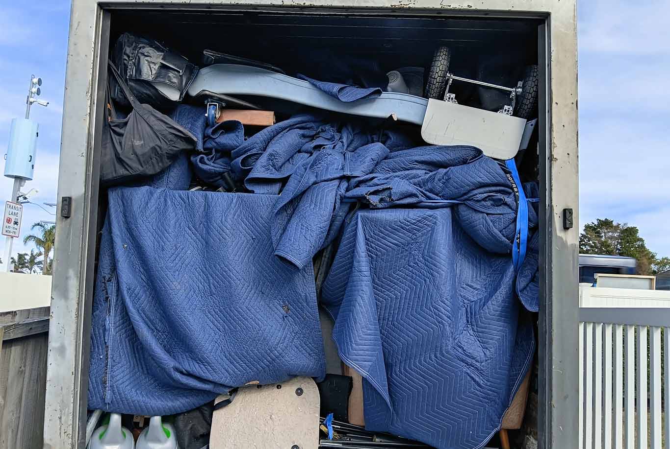 Open moving truck filled with furniture and blue moving blankets tightly packed inside.
