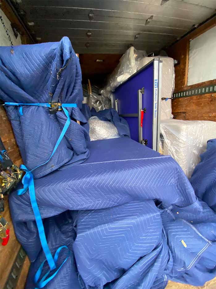Furniture wrapped in blue moving blankets and secured with blue straps inside a moving truck.