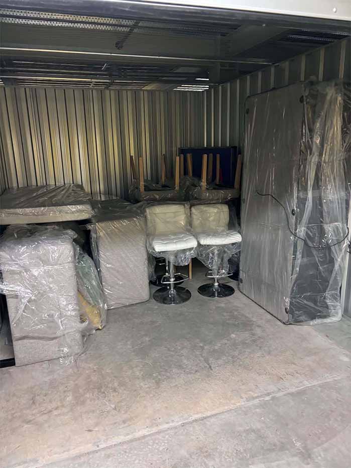 Storage unit with wrapped furniture including chairs, tables, and mattresses stacked inside.