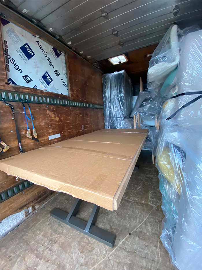 Cardboard-covered table base inside a moving van with wrapped furniture stacked on the right side.