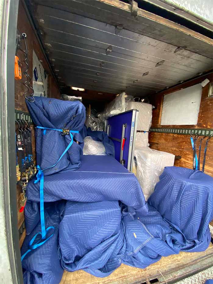 Box truck interior packed with furniture wrapped in blue moving blankets secured with straps.