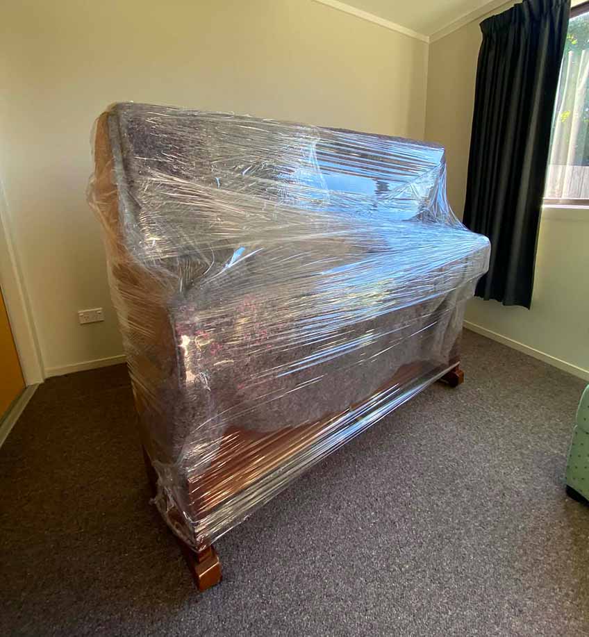Upright piano wrapped in protective plastic wrap and blankets during XMOVERS specialist piano relocation