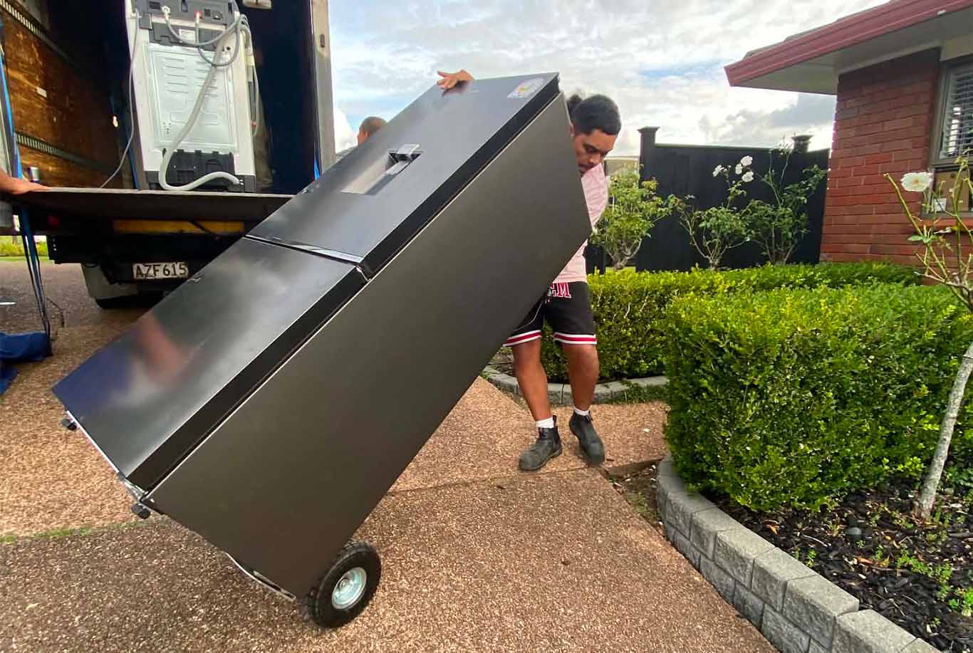 XMOVERS crew carefully unloading a large black wardrobe using tail-lift truck during house move in Auckland residential area