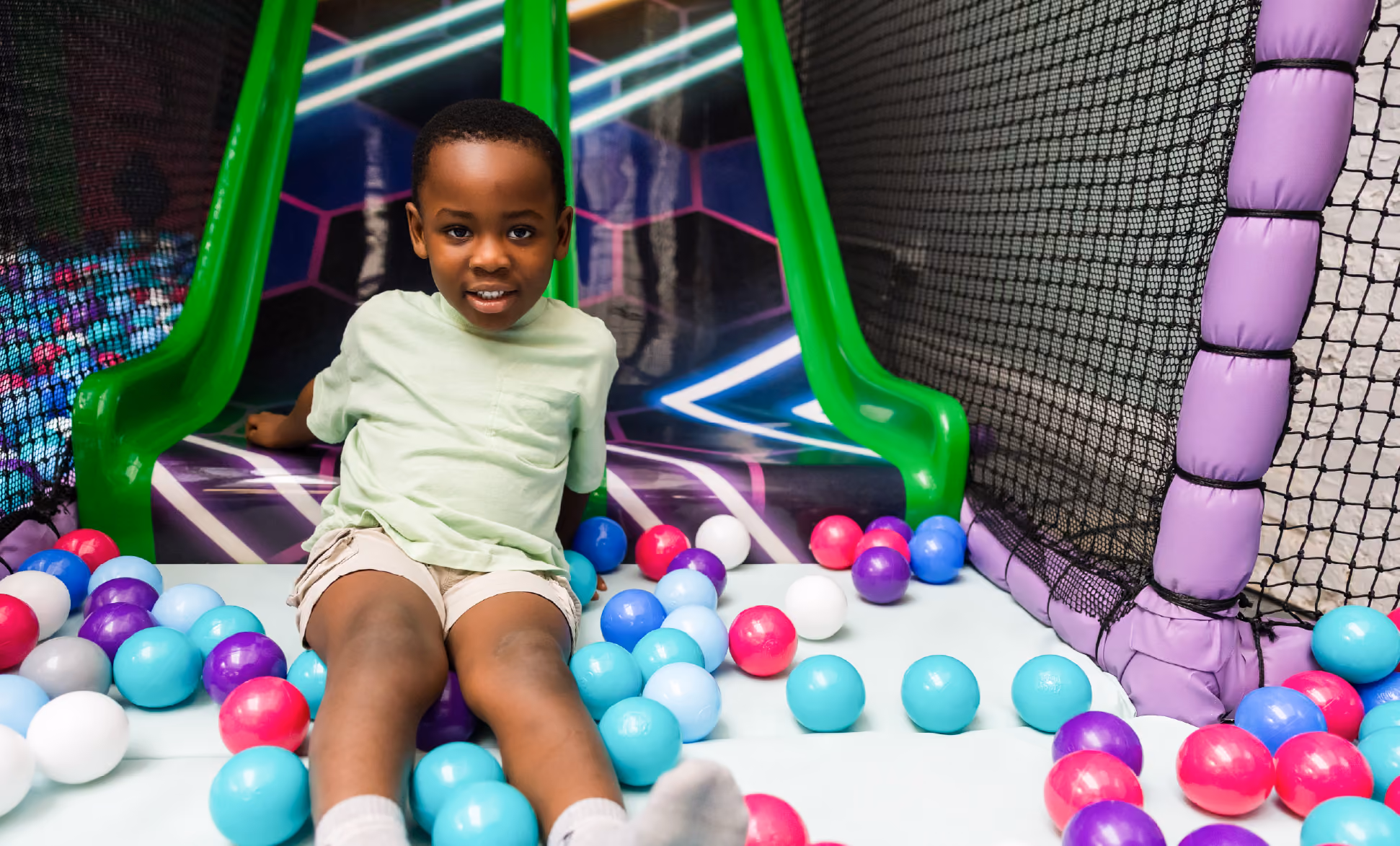 Young boy smiling and playing inside a colorful indoor soft play structure.
