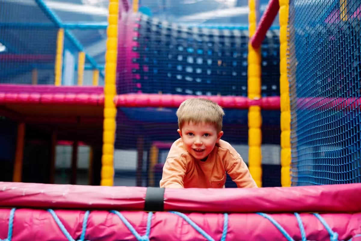 Young boy smiling and playing inside a colorful indoor soft play structure.