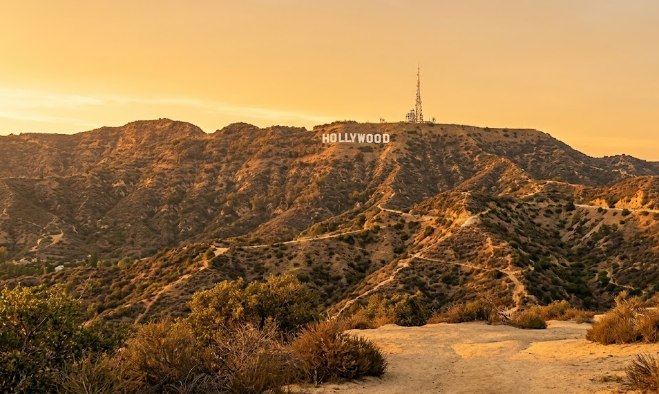 A scenic view of the Hollywood Hills at sunset, featuring the iconic Hollywood Sign on the mountain ridge, highlighting a top destination for travelers using LAX Vans group transportation.