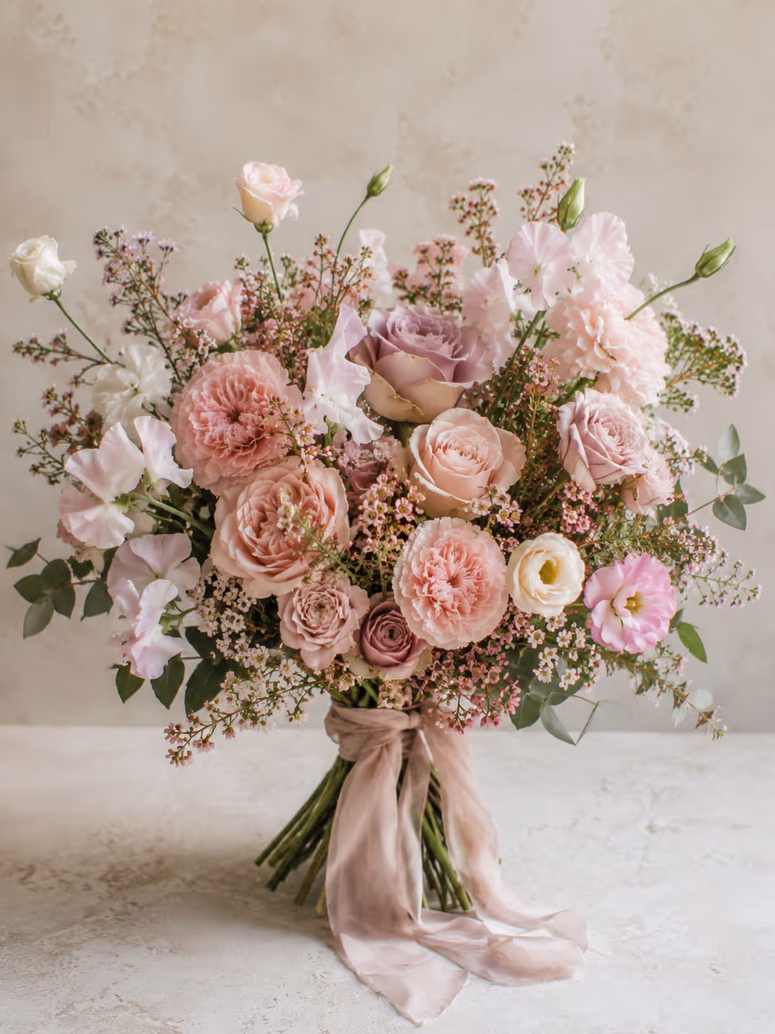 Bouquet of pink, lavender, and white flowers tied with a soft pink ribbon on a light surface.
