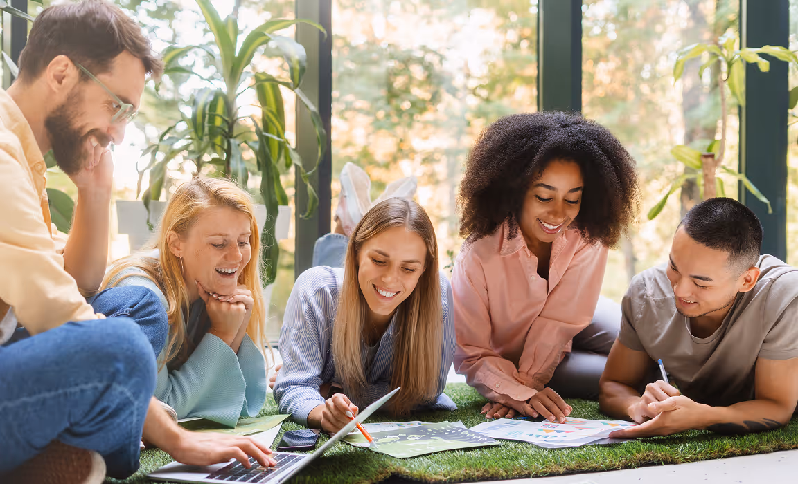 Un groupe divers de jeunes étudiants travaillant et discutant ensemble sur des documents et un ordinateur.