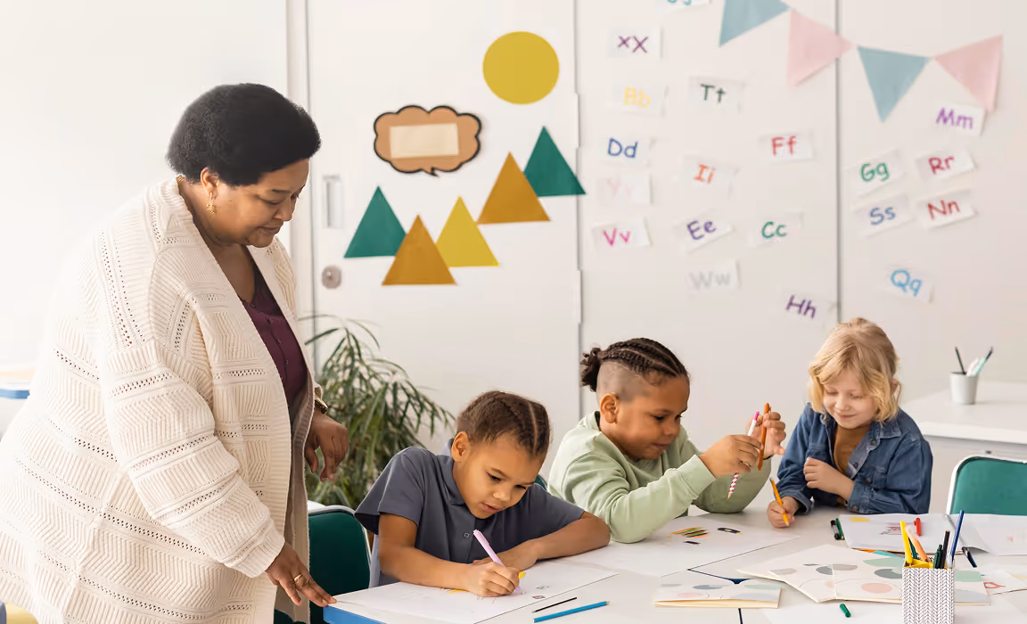 Une enseignante aide trois enfants qui dessinent et colorient à une table en classe.