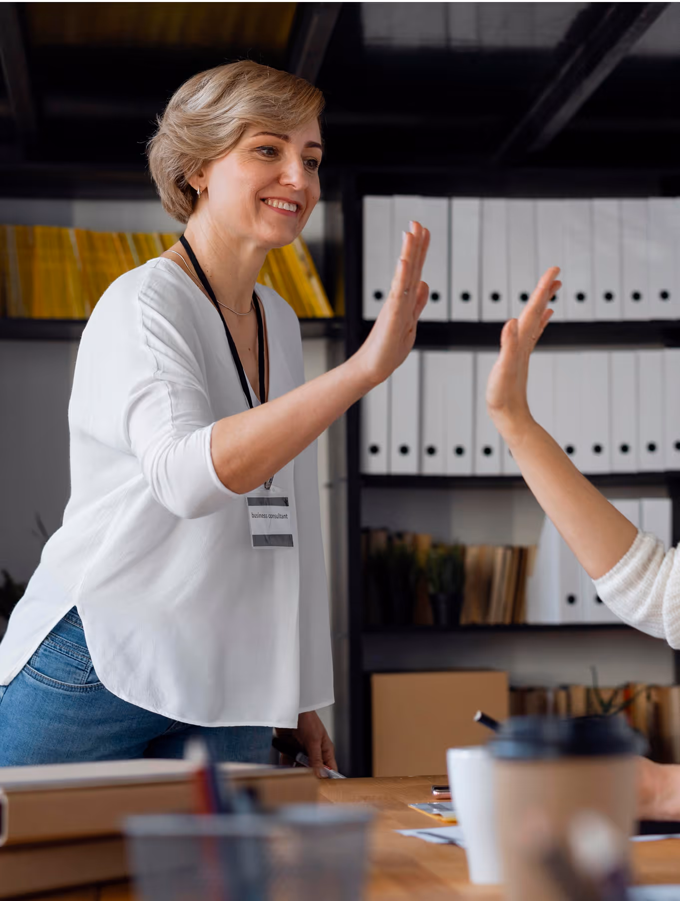 Deux personnes se donnent un high five dans un bureau avec des dossiers sur des étagères en arrière-plan.